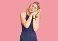 Young beautiful blonde woman wearing casual dress sleeping tired dreaming and posing with hands together while smiling with closed Royalty Free Stock Photo