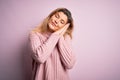 Young beautiful blonde woman wearing casual pink sweater over isolated background sleeping tired dreaming and posing with hands Royalty Free Stock Photo