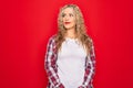 Young beautiful blonde woman wearing casual shirt standing over isolated red background smiling looking to the side and staring Royalty Free Stock Photo