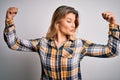 Young beautiful blonde woman wearing casual shirt standing over isolated white background showing arms muscles smiling proud Royalty Free Stock Photo