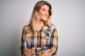 Young beautiful blonde woman wearing casual shirt standing over isolated white background smiling looking to the side and staring Royalty Free Stock Photo