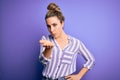 Young beautiful blonde woman wearing casual striped shirt standing over purple background looking at the camera blowing a kiss Royalty Free Stock Photo