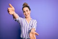 Young beautiful blonde woman wearing casual striped shirt standing over purple background looking at the camera smiling with open Royalty Free Stock Photo