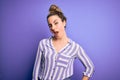 Young beautiful blonde woman wearing casual striped shirt standing over purple background winking looking at the camera with sexy Royalty Free Stock Photo