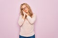 Young beautiful blonde woman wearing casual sweater and glasses over pink background sleeping tired dreaming and posing with hands Royalty Free Stock Photo