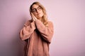 Young beautiful blonde woman wearing casual sweater and glasses over pink background sleeping tired dreaming and posing with hands Royalty Free Stock Photo