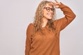 Young beautiful blonde woman wearing casual sweater and glasses over white background very happy and smiling looking far away with Royalty Free Stock Photo