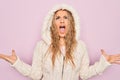 Young beautiful blonde woman wearing casual sweater with hood over isolated pink background crazy and mad shouting and yelling