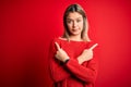 Young beautiful blonde woman wearing casual sweater over red isolated background Pointing to both sides with fingers, different Royalty Free Stock Photo