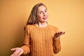 Young beautiful blonde woman wearing casual sweater standing over yellow background smiling cheerful with open arms as friendly Royalty Free Stock Photo