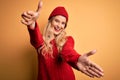 Young beautiful blonde woman wearing casual sweater and wool cap over white background looking at the camera smiling with open Royalty Free Stock Photo