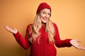 Young beautiful blonde woman wearing casual sweater and wool cap over white background smiling showing both hands open palms, Royalty Free Stock Photo