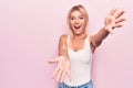 Young beautiful blonde woman wearing casual t-shirt standing over isolated pink background looking at the camera smiling with open Royalty Free Stock Photo