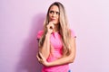 Young beautiful blonde woman wearing casual t-shirt standing over isolated pink background thinking concentrated about doubt with Royalty Free Stock Photo