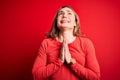 Young beautiful blonde woman wearing casual t-shirt standing over isolated red background begging and praying with hands together Royalty Free Stock Photo