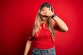 Young beautiful blonde woman wearing casual t-shirt standing over isolated red background covering eyes with hand, looking serious Royalty Free Stock Photo