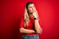 Young beautiful blonde woman wearing casual t-shirt standing over isolated red background with hand on chin thinking about Royalty Free Stock Photo