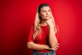 Young beautiful blonde woman wearing casual t-shirt standing over isolated red background with hand on chin thinking about Royalty Free Stock Photo