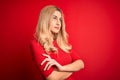 Young beautiful blonde woman wearing casual t-shirt standing over isolated red background looking to the side with arms crossed Royalty Free Stock Photo