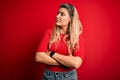 Young beautiful blonde woman wearing casual t-shirt standing over isolated red background looking to the side with arms crossed Royalty Free Stock Photo