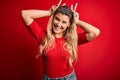 Young beautiful blonde woman wearing casual t-shirt standing over isolated red background Posing funny and crazy with fingers on Royalty Free Stock Photo