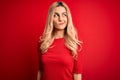 Young beautiful blonde woman wearing casual t-shirt standing over isolated red background smiling looking to the side and staring Royalty Free Stock Photo