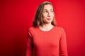 Young beautiful blonde woman wearing casual t-shirt standing over isolated red background smiling looking to the side and staring Royalty Free Stock Photo