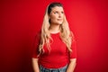 Young beautiful blonde woman wearing casual t-shirt standing over isolated red background smiling looking to the side and staring Royalty Free Stock Photo