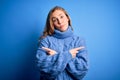 Young beautiful blonde woman wearing casual turtleneck sweater over blue background Pointing to both sides with fingers, different Royalty Free Stock Photo