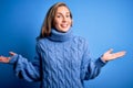 Young beautiful blonde woman wearing casual turtleneck sweater over blue background smiling showing both hands open palms, Royalty Free Stock Photo