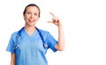 Young beautiful blonde woman wearing doctor uniform and stethoscope smiling and confident gesturing with hand doing small size Royalty Free Stock Photo