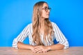 Young beautiful blonde woman wearing glasses sitting on the table looking to side, relax profile pose with natural face with Royalty Free Stock Photo