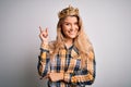 Young beautiful blonde woman wearing golden crown of queen over isolated white background with a big smile on face, pointing with Royalty Free Stock Photo