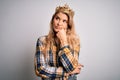 Young beautiful blonde woman wearing golden crown of queen over isolated white background with hand on chin thinking about Royalty Free Stock Photo