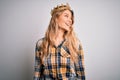 Young beautiful blonde woman wearing golden crown of queen over isolated white background looking away to side with smile on face, Royalty Free Stock Photo