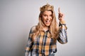 Young beautiful blonde woman wearing golden crown of queen over isolated white background pointing finger up with successful idea Royalty Free Stock Photo