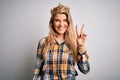 Young beautiful blonde woman wearing golden crown of queen over isolated white background smiling with happy face winking at the Royalty Free Stock Photo