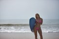 Young, beautiful, blonde woman, wearing a pink bikini, posing with a blue surfboard under her arm, in sensual and provocative Royalty Free Stock Photo