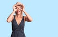 Young beautiful blonde woman wearing summer hat and dress doing ok gesture like binoculars sticking tongue out, eyes looking Royalty Free Stock Photo