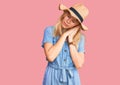 Young beautiful blonde woman wearing summer hat and dress sleeping tired dreaming and posing with hands together while smiling Royalty Free Stock Photo