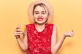 Young beautiful blonde woman wearing summer hat drinking glass of orange juice screaming proud, celebrating victory and success Royalty Free Stock Photo