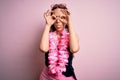 Young beautiful blonde woman wearing swimsuit and floral Hawaiian lei over pink background doing ok gesture like binoculars Royalty Free Stock Photo