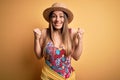 Young beautiful blonde woman wearing swimsuit and summer hat over yellow background excited for success with arms raised and eyes Royalty Free Stock Photo