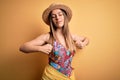 Young beautiful blonde woman wearing swimsuit and summer hat over yellow background stretching back, tired and relaxed, sleepy and Royalty Free Stock Photo