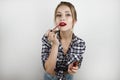 Young beautiful blonde woman wearing trendy checkered shirt and denim shorts applying red lipstick isolated white Royalty Free Stock Photo