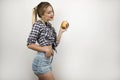 Young beautiful blonde woman wearing trendy checkered shirt and denim shorts holding fresh tasty apple isolated white Royalty Free Stock Photo