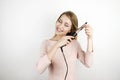 Young beautiful blonde woman wearing trendy pink dress using curling iron to make fashionable hairstyle by herself on Royalty Free Stock Photo