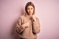 Young beautiful blonde woman wearing winter wool sweater over pink isolated background In hurry pointing to watch time,