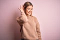 Young beautiful blonde woman wearing winter wool sweater over pink isolated background smiling with hand over ear listening an Royalty Free Stock Photo