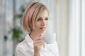 Young beautiful blonde woman in white shirt and glasses is sitting on the sofa in bright office against the window Royalty Free Stock Photo